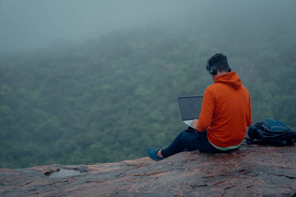 Digital nomad working on a laptop at a sunlit outdoor cafe with mountains in the background